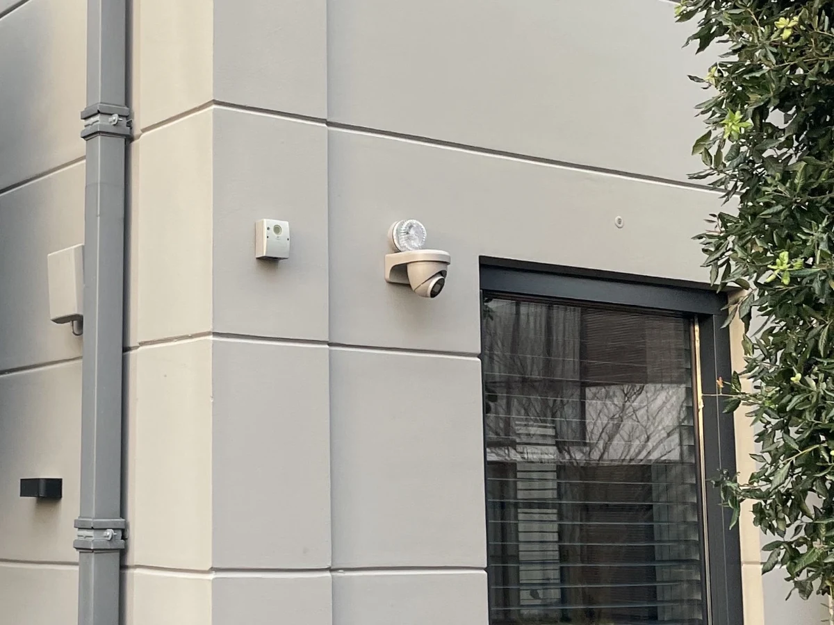 Detail van een camera en een sensor die zijn meegespoten in de kleur van de gevel