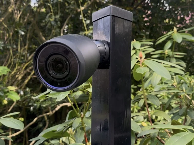 Zwarte camera op een paal in de beplanting, gericht op de erfgrens