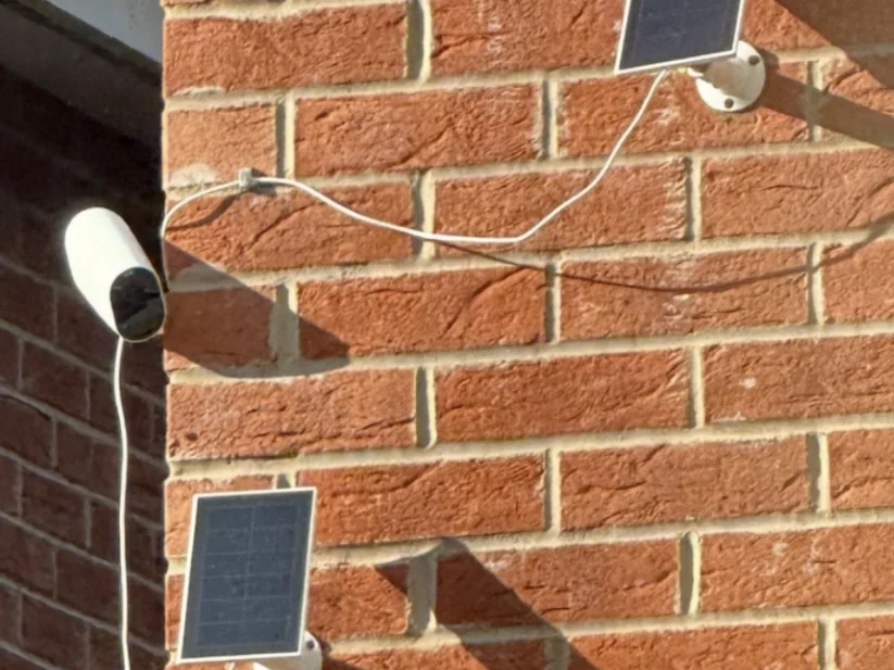 Accucamera met twee losse zonnepaneeltjes en snoeren in bochten over het metselwerk