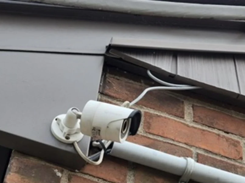 Camera bij de dakrand met een witte kabel los over het metselwerk