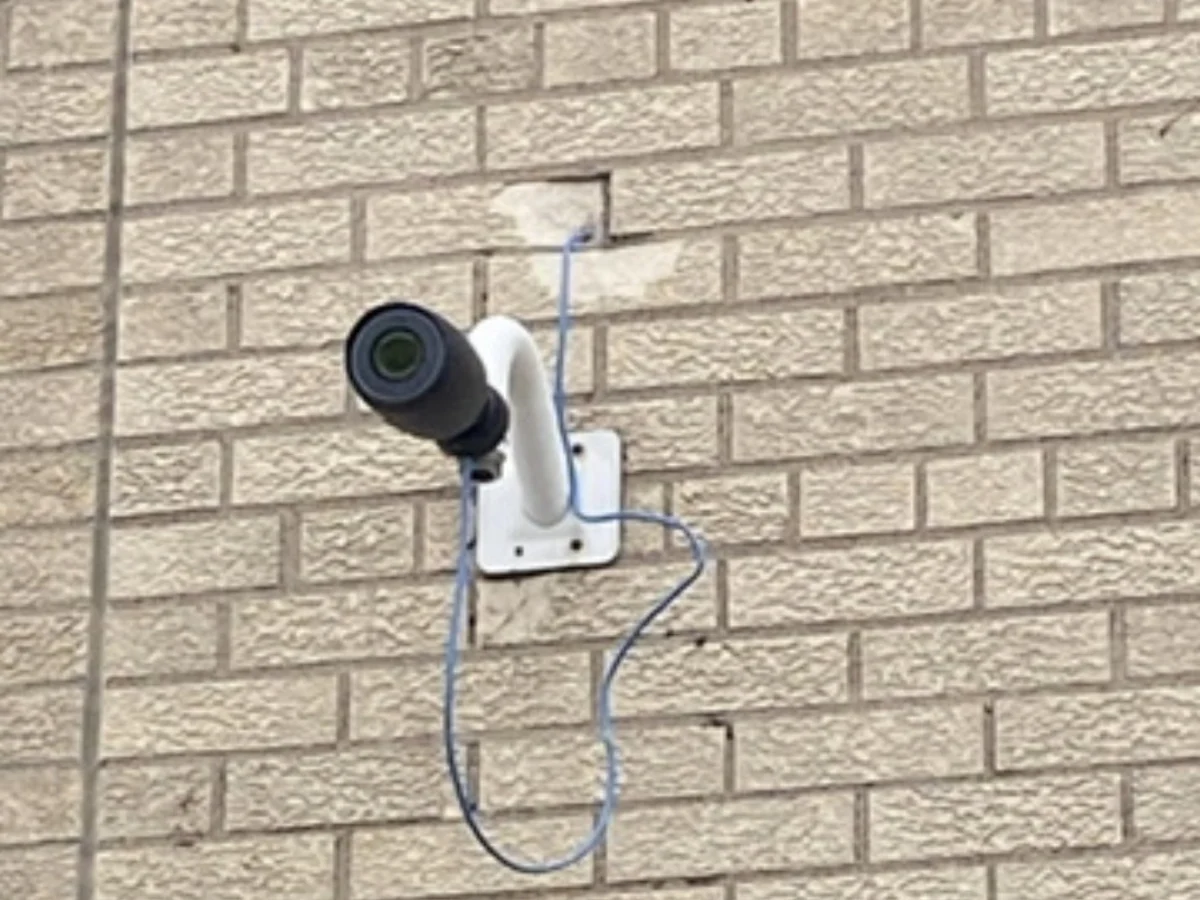 Camera op een beugel met een lichtblauwe netwerkkabel in slappe lussen over de gevel
