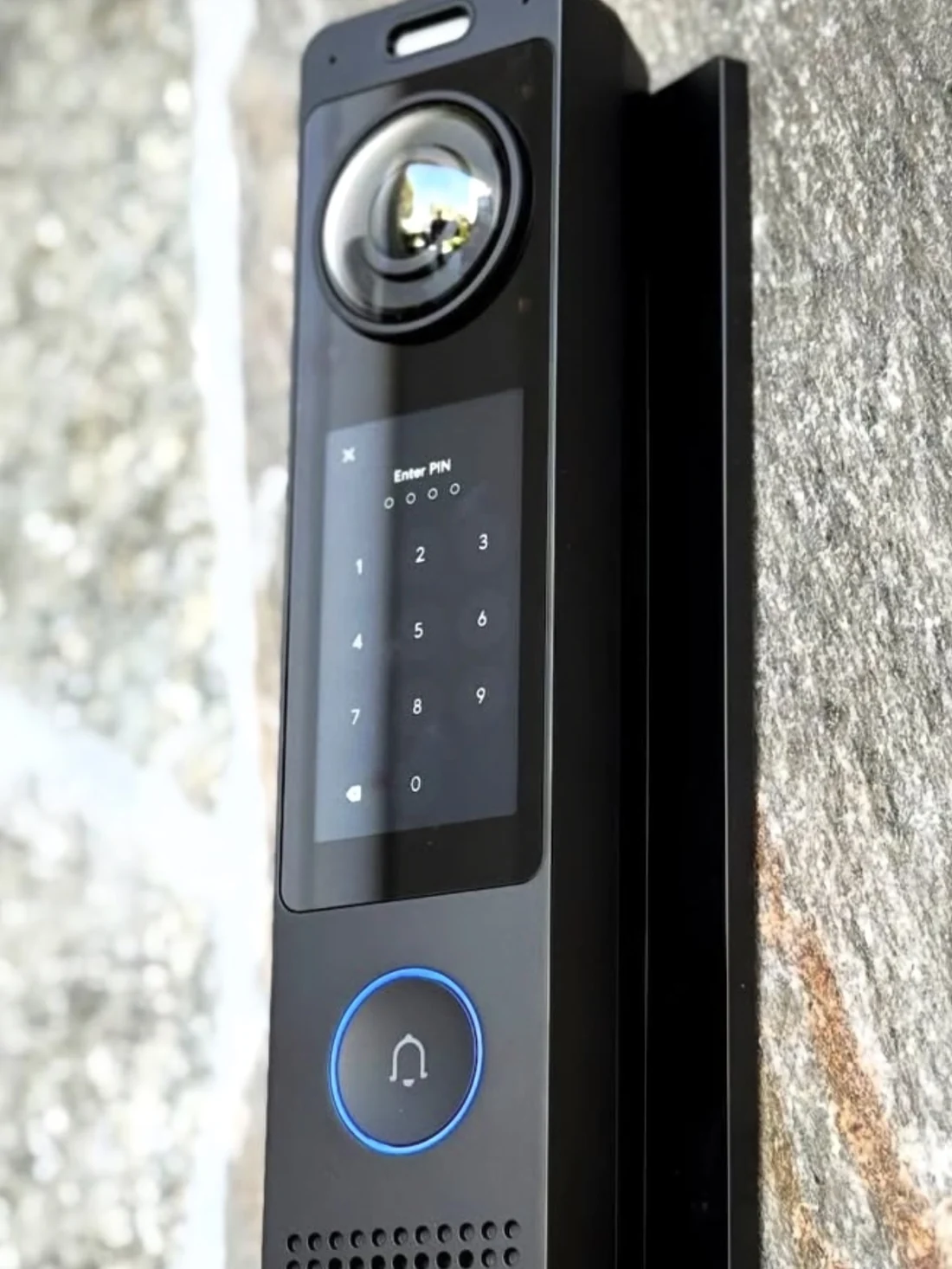 Zwarte video-intercom met scherm en pincode-toetsenbord tegen een natuurstenen gevel