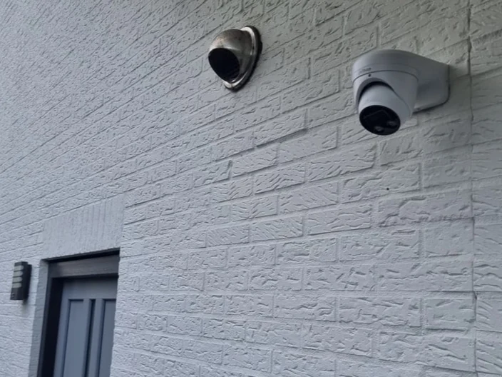 Nieuwe dome-camera op een geschilderde gevel, naast de oude weggeroeste behuizing