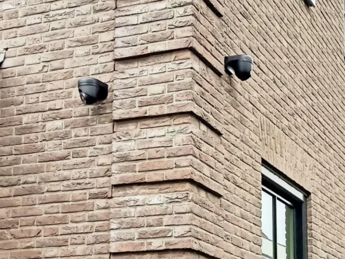 Twee camera&rsquo;s op de hoek van een gevel, kabels binnendoor