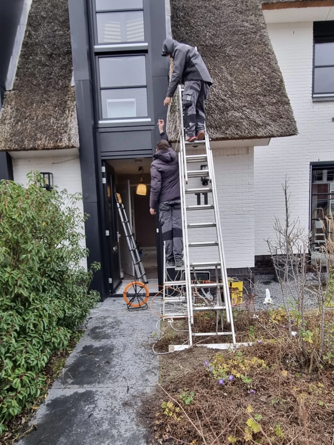 Twee monteurs op de ladder aan het werk bij een woning met rieten kap
