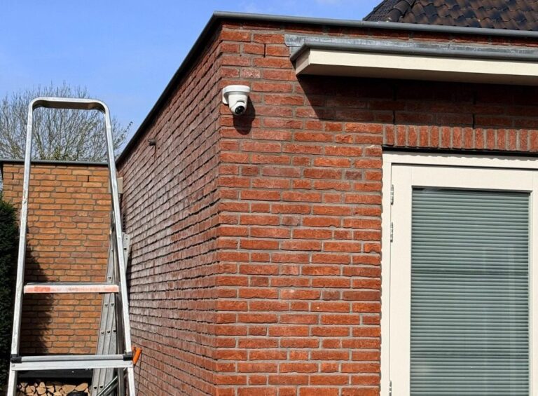 Witte camera hoog op de hoek van een aanbouw van rode baksteen, met een trapladder ernaast