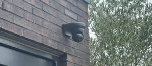 Zwarte camera op een zwarte beugel boven een donkere deur in een gevel van donkere baksteen
