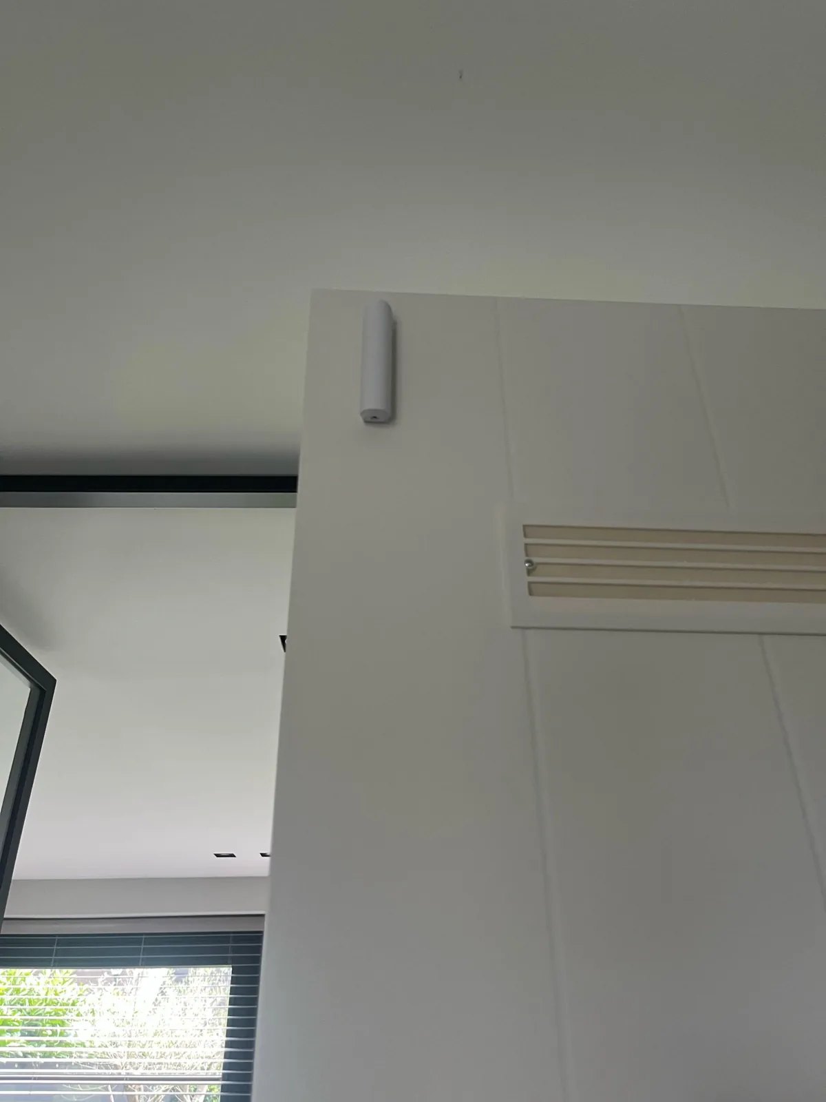 Wit Ajax-contact boven aan een witte binnendeur met een ventilatierooster