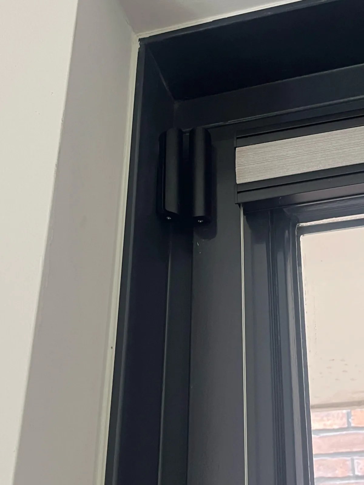 Zwart Ajax-deurcontact van twee delen boven in een zwart deurkozijn, naast een lichte muur