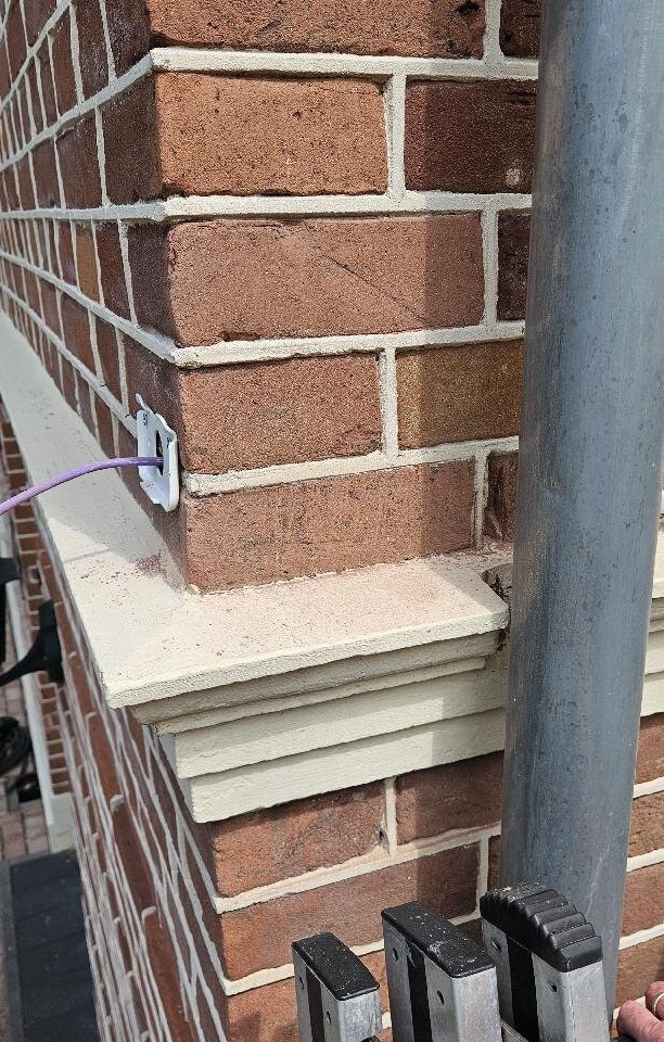 Paarse netwerkkabel die via een kleine witte doorvoer in het metselwerk verdwijnt, vlak boven een stenen dorpel van een klassieke woning