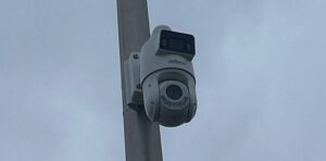 Witte camera met een vaste bovenlens en een draaibare onderlens aan een grijze mast