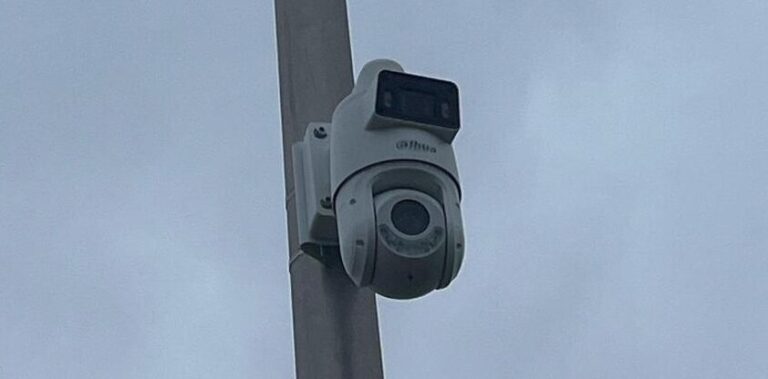 Witte camera met een vaste bovenlens en een draaibare onderlens aan een grijze mast