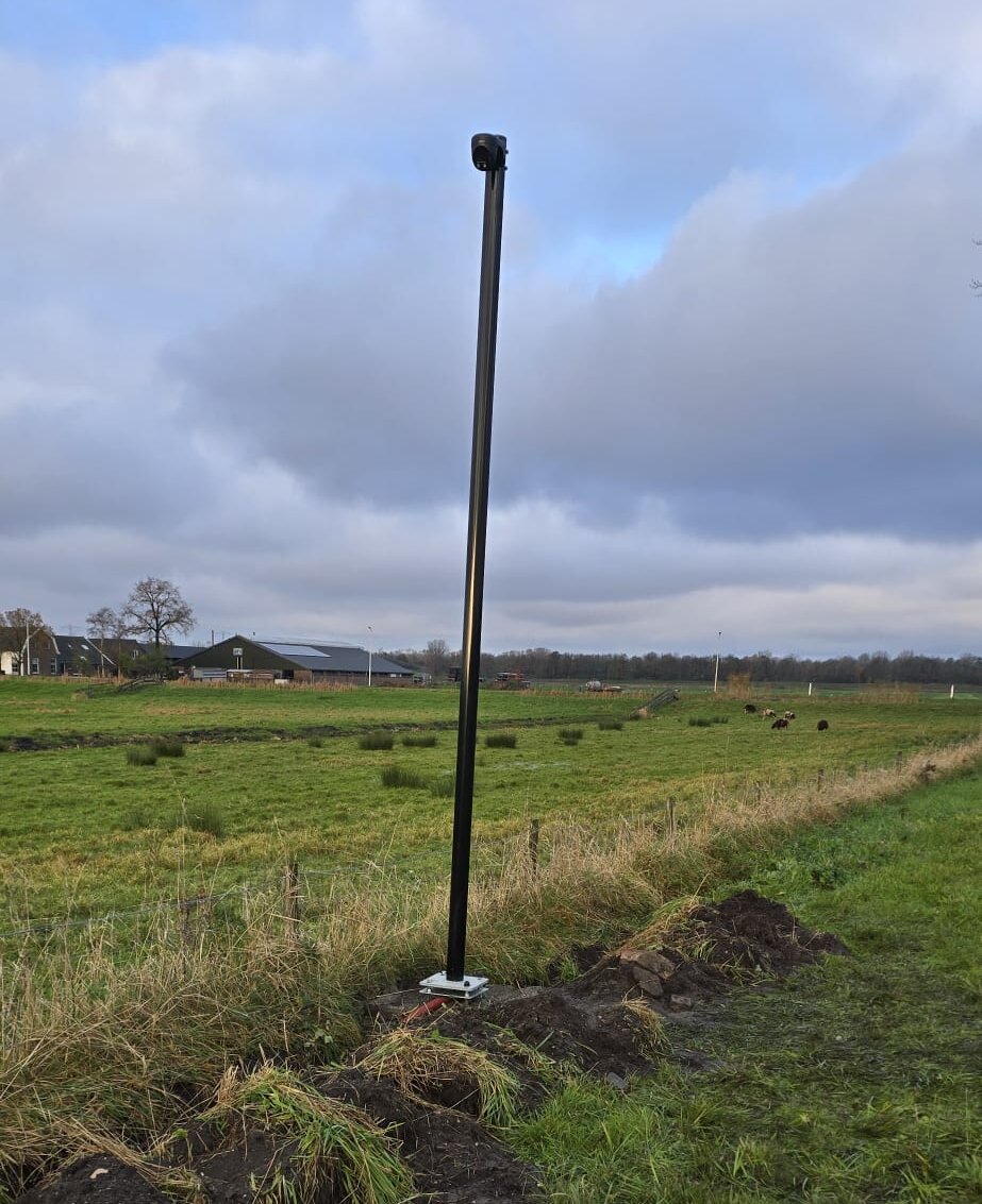 Zwarte cameramast in het open veld onder een bewolkte lucht