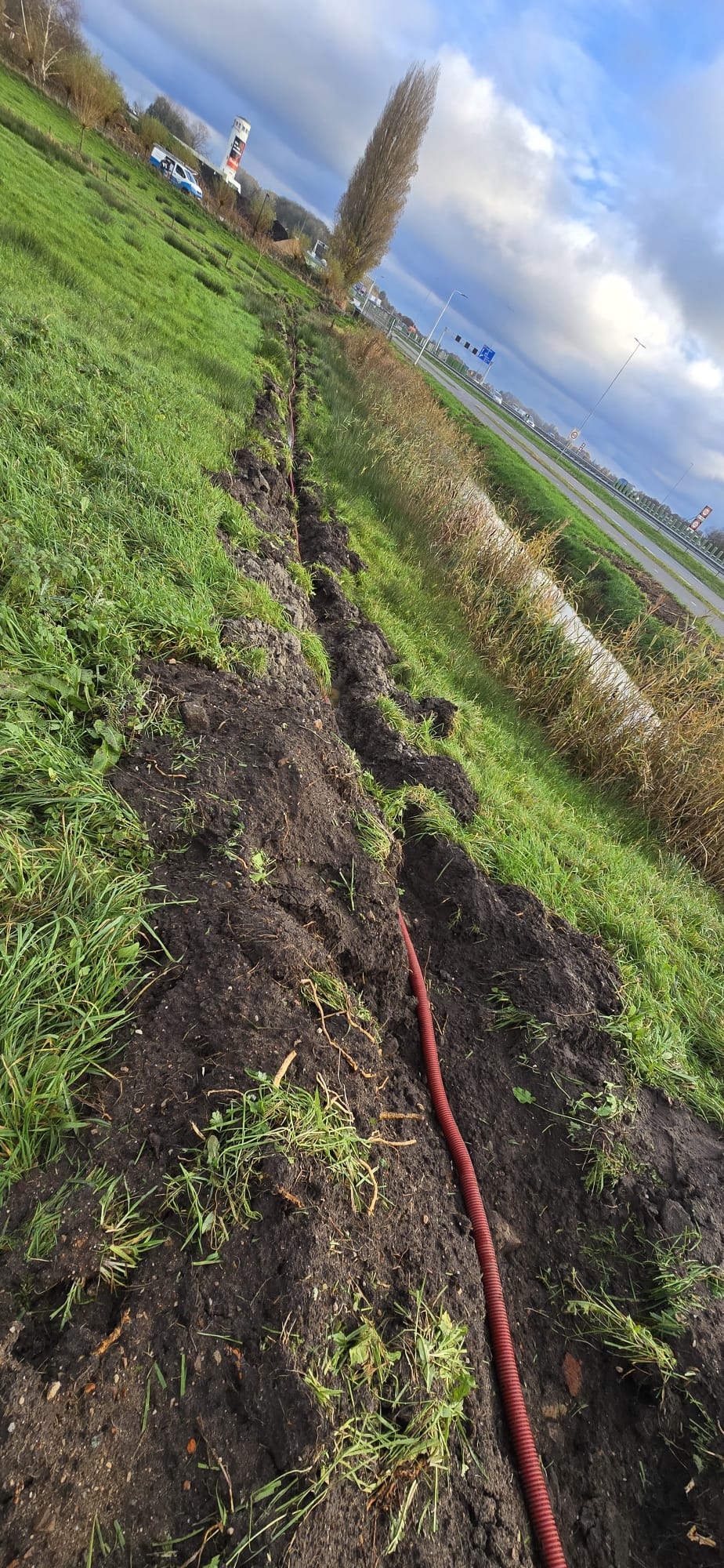 Lange open sleuf door het gras met een rode mantelbuis erin
