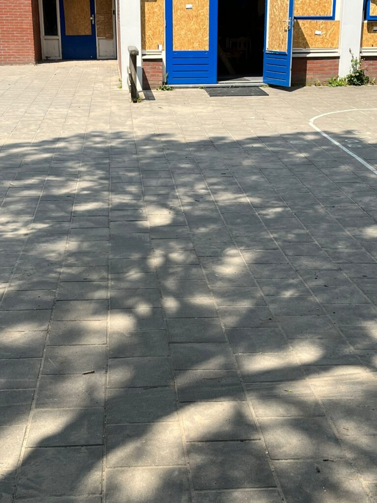 Bestraat schoolplein met blauwe deuren en ramen die met houten platen zijn dichtgezet