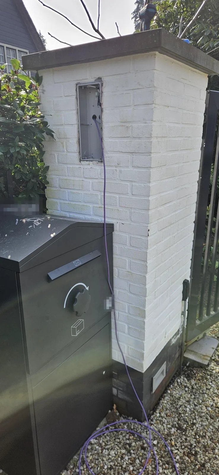 Witte gemetselde pilaar naast een zwart hek, met een lege inbouwdoos waar een paarse netwerkkabel binnenkomt