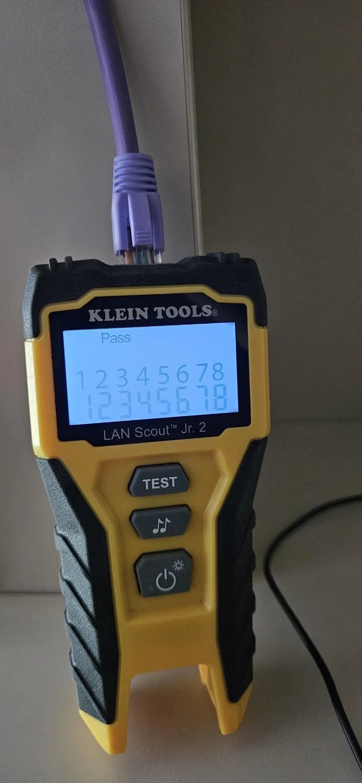 Gele kabeltester met een paarse netwerkkabel erin, het scherm toont Pass en de cijfers een tot en met acht
