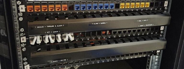 Drie patchpanelen met oranje, blauwe, gele en witte aansluitingen en zwarte labels met de kleurcode per systeem
