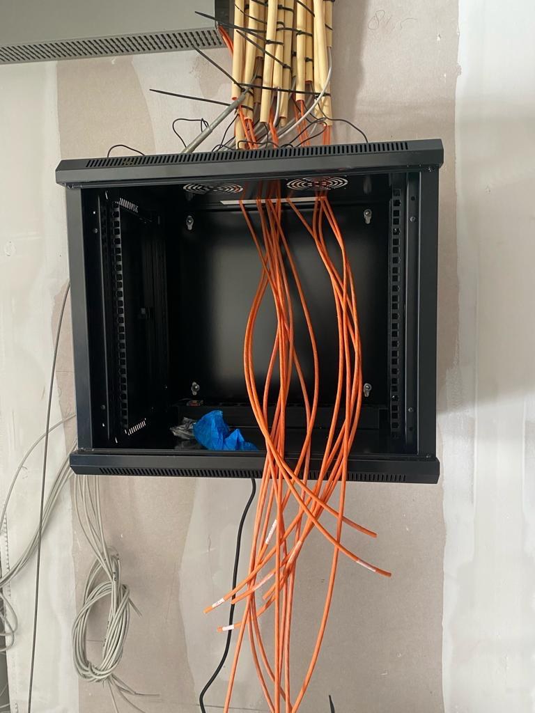Lege zwarte wandkast tegen een kale muur, met een bundel oranje kabels die van boven binnenkomt