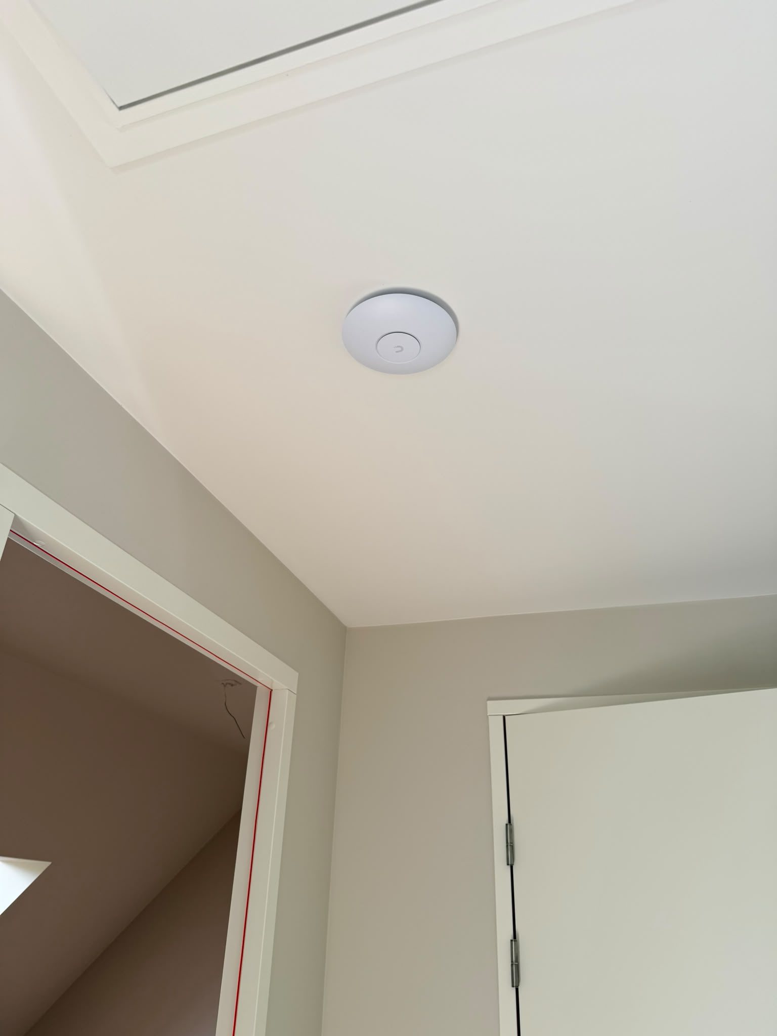Witte wifi-zender aan het plafond van een overloop, zonder zichtbare kabel