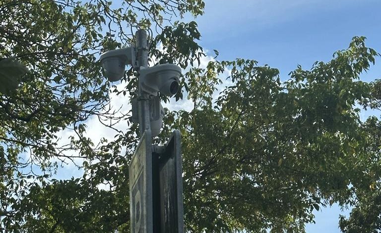 Witte camera's op beugels bovenaan een mast boven een verkeersbord, met bomen en lucht erachter