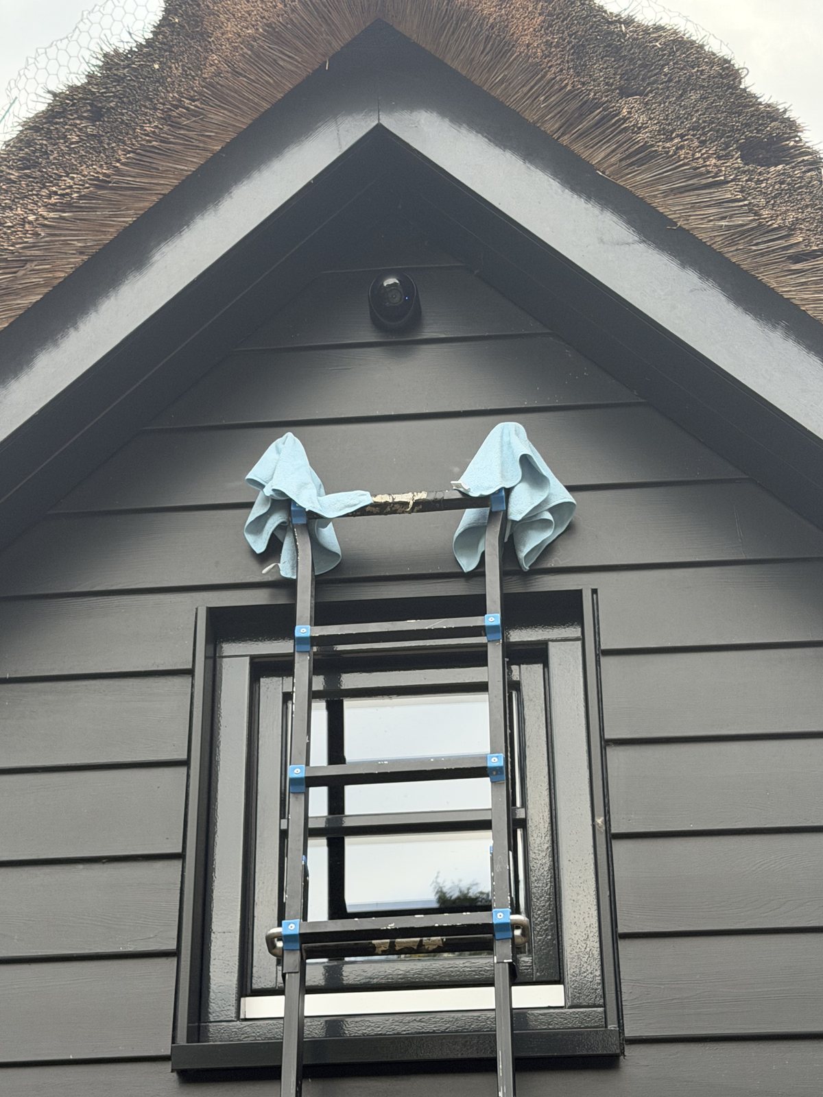 Ladder tegen een donkere houten gevel met lichtblauwe doeken over de bovenkant