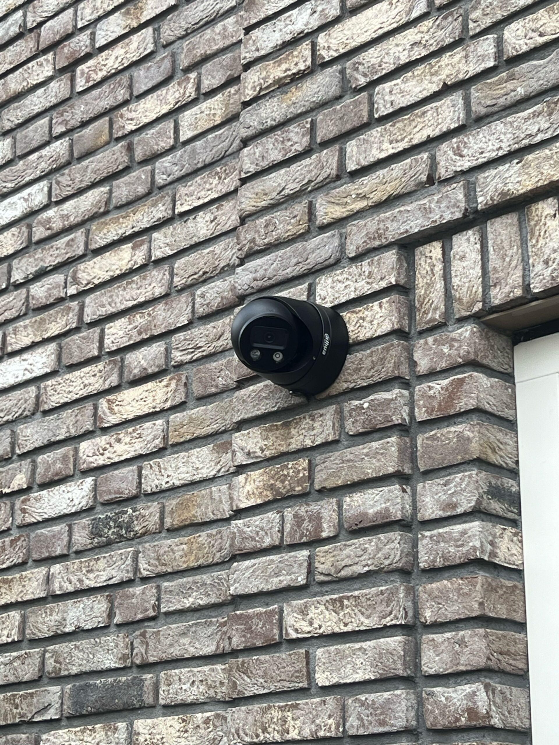 Zwarte camera van dichtbij op metselwerk naast een wit kozijn