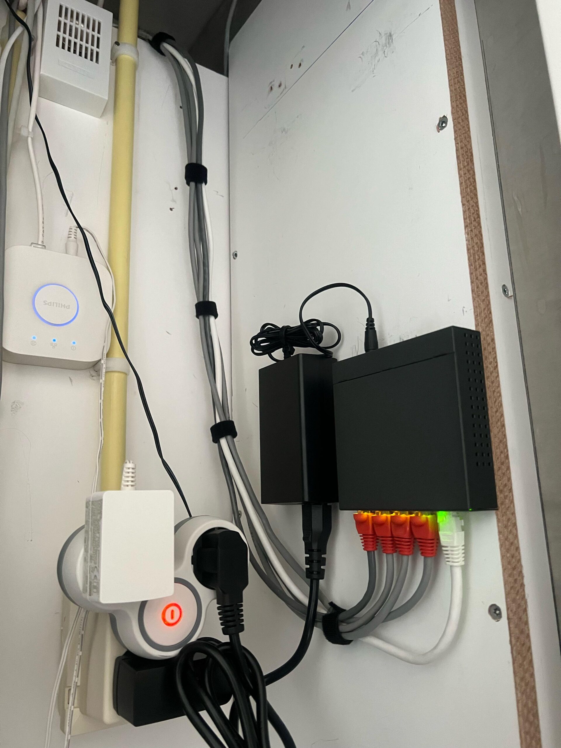 Kleine zwarte switch in een witte kast, met vier netwerkkabels met oranje stekkers en een witte kabel
